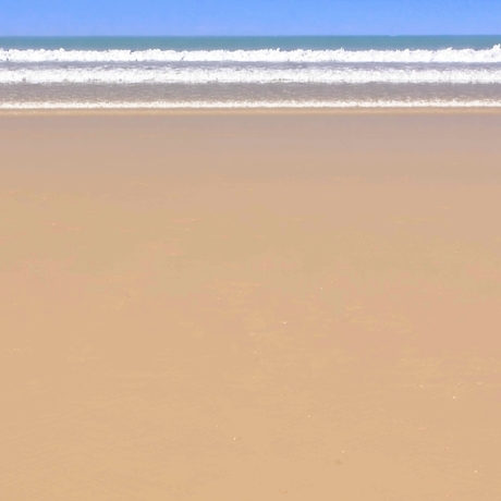 the photograph shows a smooth sandy beach on a sunny day with three waves breaking the shore