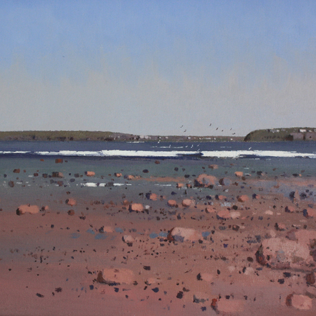 Beach scene with rocks and surf under a blue sky.