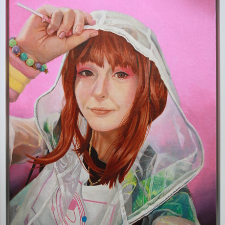 Portrait of a young woman with an enigmatic smile against a bubblegum pink background. She wears a semi-transparent white jacket with a raised hood and holds the front of with a raised hand into which is tucked a lollipop.  Under the jacket she wears a white t-shirt with a revolving planets motif.