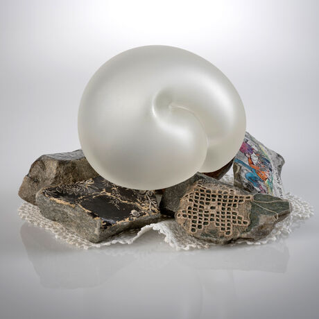 Rebecca has sculped an embryotic glass form to represent the innocence and fragility of life.
The glass form has been etched giving the glass a satin texture.
 She has incorporated rocks and stones, found objects such as images and fabric found in the family home. 
The embriotic form rests delicately on this mound of rubble exposed to the outside elements.
