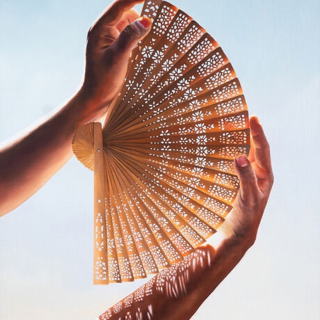 Hand holding an intricate fan with light streaming through the fan, casting a pattern of shadows across the hand.