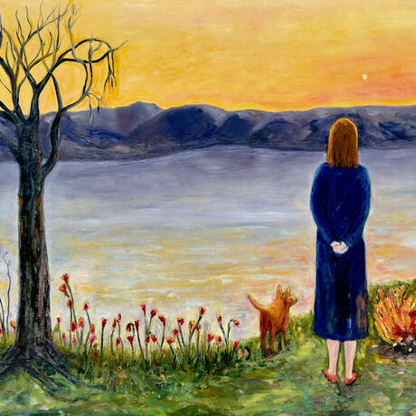 A woman and her animal companion look across water to the mountains and evening sky