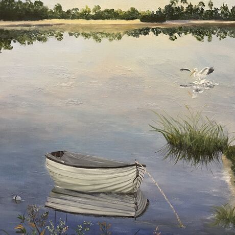 Pelicans fly overhead  and a boat is reflected in still water with reeds on the shore.