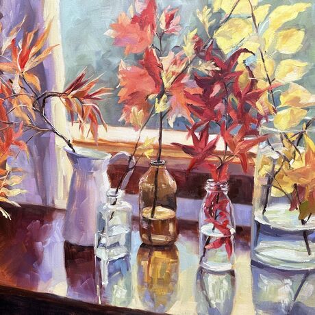 Autumn leaves of red, orange and yellow, placed into vessels of various shapes and sizes on a table in front of a window.

