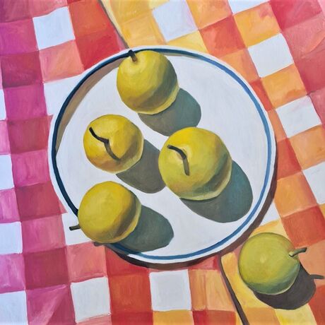 Looking down onto a plate of light green nashi pears sitting on a brightly checked oink, orange and yellow tablecloth.