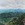 Brilliant clouds over distant blue mountains, with forested ridges, green pastures, and flowering rainforest foliage in the foreground.  