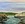 The image shows a full moon rising over a rocky limestone cove in the early evening light.