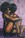 A young black woman with a very large afro sits naked on the floor. Her arms hanging over a lifted knee, she covers her femininity from the viewer. 