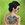 A woman stands against a vibrant green background. On her back is a large bull tattoo. Her hair is black and her cheeks and nose are rosy red. She looks over her shoulder with a disproportionately large eye. Her expression is sad.