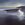 A tonal painting of a beach at sunset. The sky is glazed in golden yellow from bottom right moving towards darkening blues at the top and left. 

The sand is dark brown shadow with a tidal stream in golden reflected light cutting down the right. where the dark blue ocean meets the beach, the reflections are blue moving to golden in the foreground. The bottom third of the painting is more detailed with detail of seaweed and water ripples in the tidal stream that sweep towards the waters edge. 