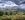 Green trees and a touch of a blue loch, or lake, with a mountain in the distance under a grey, lowering, thundery sky.