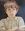 A young middle eastern boy, arms folded as he sullenly gazes out of the shadows of a doorway.