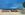 Clear blue sky with a few clouds, ocean view with a row of rocks that people have decorated and tree on the right side with shadows on a walkway 