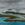 Storm clouds over a mountainous island. Waves roll onto the beach. 