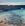 Seagulls fly over shallow water and rocks at the beach ona sunny day.