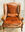 A velvet, rust coloured french provincial chair in the sunlight on a parquetry style floor, with a Provencal blue french door behind