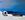 white grecian pot and an old Greek fishing boat sitting on top of a whitewashed building on Santorini overlooking the deep blue water of the caldera in the Mediterranean Sea 