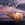 A painting of a stag elk walking through a mysterious, foggy, dark cloudscape surrounded by hues of purple.