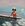 A woman in a red swimsuit and white floppy hat sailing in a canoe. A pastel pink and blue background.