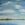 big sky with white clouds over a hill and reflected in a lake