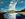 White clouds rising dramatically from the coastline with a blue sky, shoreline and reflected clouds in the water.