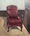 This is an old armchair with faded maroon upholstery in an interior.