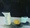 A jug and a mug, both in shades of blue-grey sit atop a table with a yellow/green lemon. The background is black