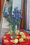 Transparent glass vase with bluebells surrounded by quinces on the red cloth; the mirror on the background reflects female portrait on the wall.