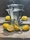 Yellow lemons against a grey backdrop, reflected in a bialetti silver coffee pot