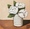 Soft white roses in a small white vase with a warm toned neutral background