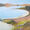 A curving bay with a view back across the lagoon to beach dunes and a foreground with low coastal plants. 