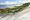 An ocean scene, sparkling water in the distance and beach scrub in the foreground.