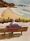 An artwork showing an elderly man sitting on a bench at a lookout over the white sands of a sunny beach .