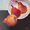 A knife painting of three red and gold coloured pears spilled out of a deep white bowl on a dark background.