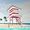 A fun, eye catching artwork with a bright red and white lifeguard tower on a beach with two women reacting as entering the cool water