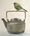 New Zealand Bellbird perches on the woven handle of a rustic pottery kettle.