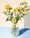 Yellow flowers in spotted glass vase on blue background