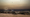 Car relic on rocky beach with cityscape background under a toxic sky