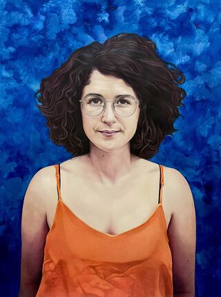 A woman, Madeleine Parry, wearing an orange top and glasses smirking in front of a blue glittery background.