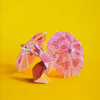 An origami bunny standing amongst cocktail parasols against a yellow background