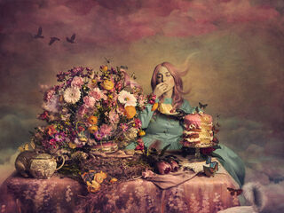 A woman sits at a dutch inspired still life table. She has pink hair and is wearing a blue dress. There is a layered pink cake in front and she is eating a piece of it. She is Alice in wonderland all grown up and there is a cat, rabbit and butterflies in the image. The background is a pink and blue sunrise. 