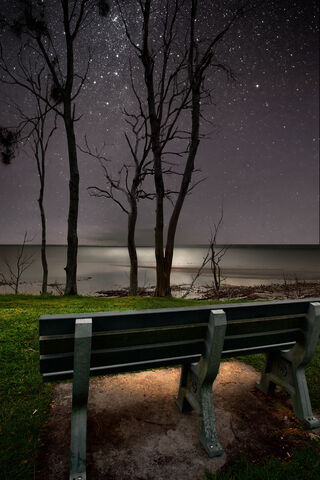 Moody image of a bench on a cliff overlooking the sea at night. 