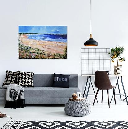 Long and wide beach. People walking on the sand. People sitting under umbrellas. Others sitting on the sand. Greenery and wild flowers on the foreground. Hills in the horizon. 