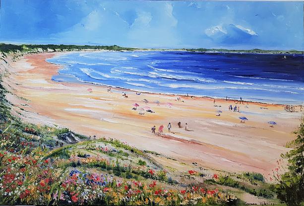 Long and wide beach. People walking on the sand. People sitting under umbrellas. Others sitting on the sand. Greenery and wild flowers on the foreground. Hills in the horizon. 