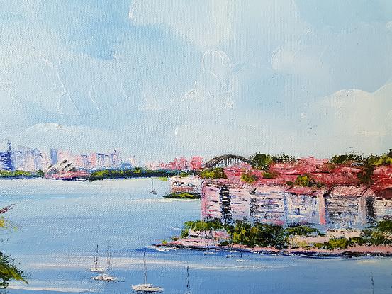 View of Sydney Harbour from Point Pier. Sydney skyline in the background. White blocks of units with red tile roofs in the middle ground. Trees and wild flowers in the foreground. Boats in the water in the middle. 