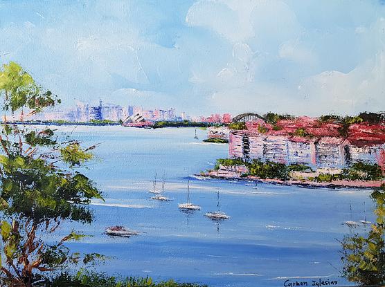 View of Sydney Harbour from Point Pier. Sydney skyline in the background. White blocks of units with red tile roofs in the middle ground. Trees and wild flowers in the foreground. Boats in the water in the middle. 