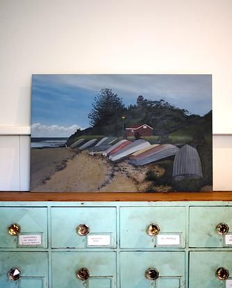 A row of dinghies resting on the foreshore of Long Reef Basin at Fishermans Beach. 
The ocean in the back ground and a bush covered headland framing the fisherman's hut. 