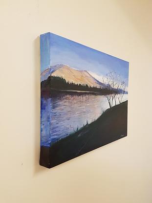 Cool blue landscape with dark foreground and  silhouette of trees. There are purple and pinks in the mountain behind the lake and in the reflections in the lake.