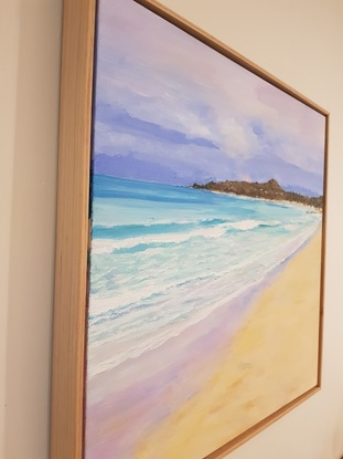 A view across sand with turquoise water and waves. There are small inviting waves and distant deep blue water.  The tiny lighthouse is in the background set against a darkish sky with white clouds and the peninsula at dusk.