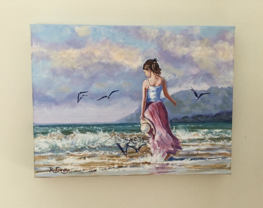 Woman in long dress walking on beach with seagulls flying nearby 